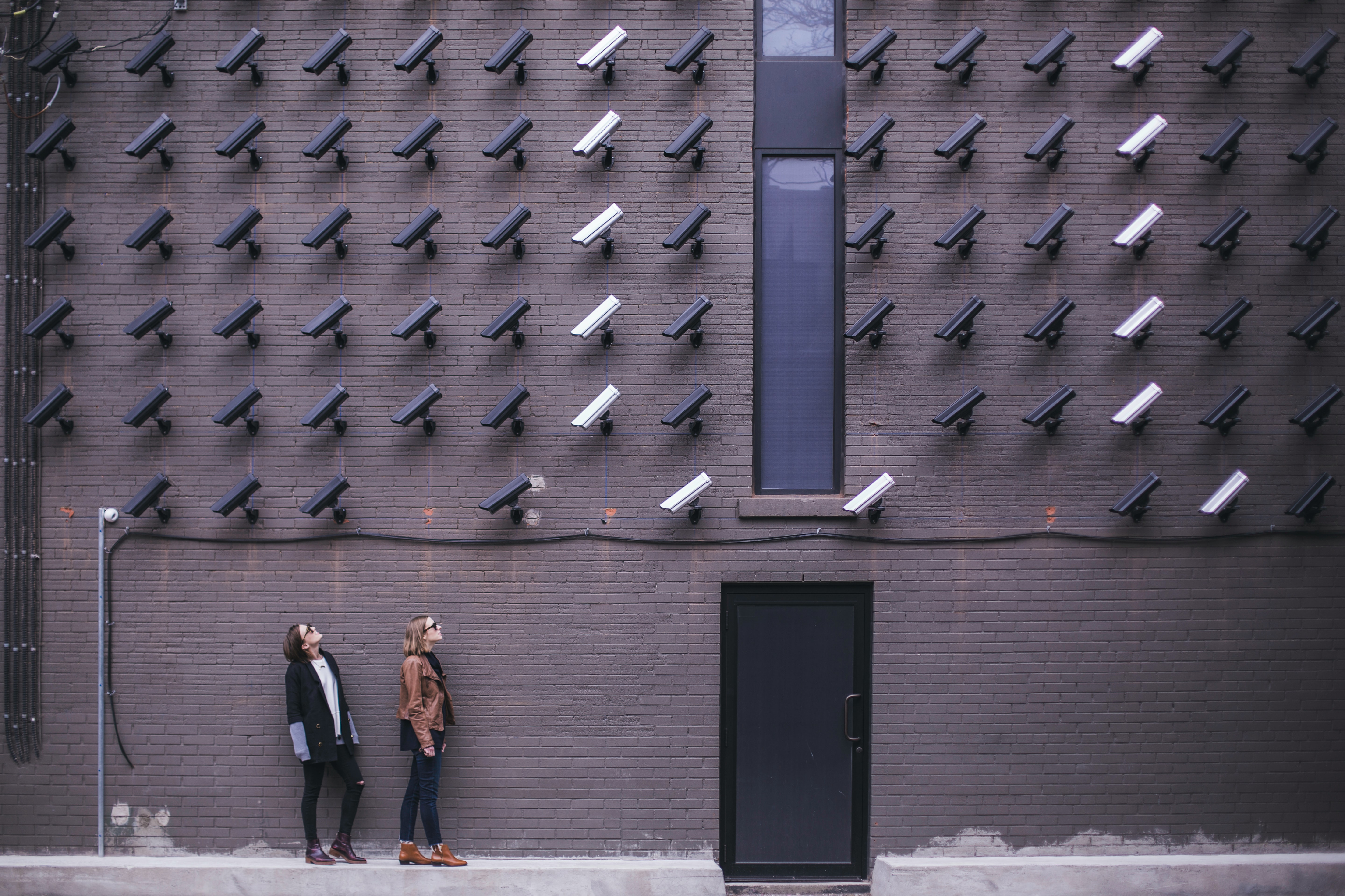 Lots of cameras attached to a building watching people walking down the street